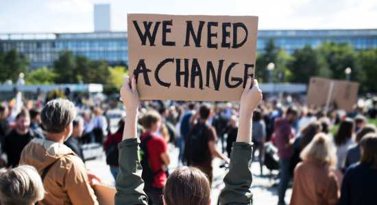 Woman holding a sign stating 'We need change'
