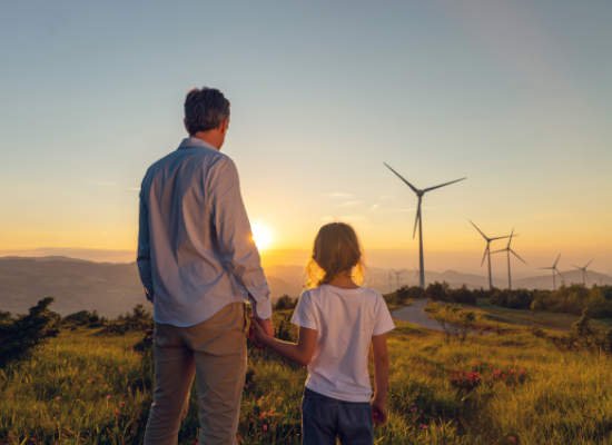 father and daughter looking at a sunset and wind turbines.