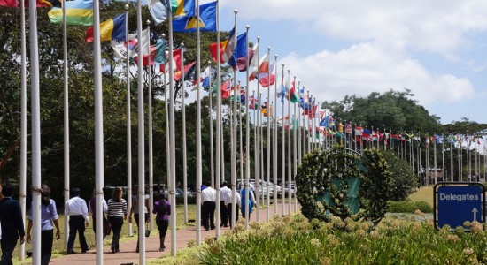 An outdoor view of the Nairoba UNEP headquarter with delegates walking through a path paved with flag poles