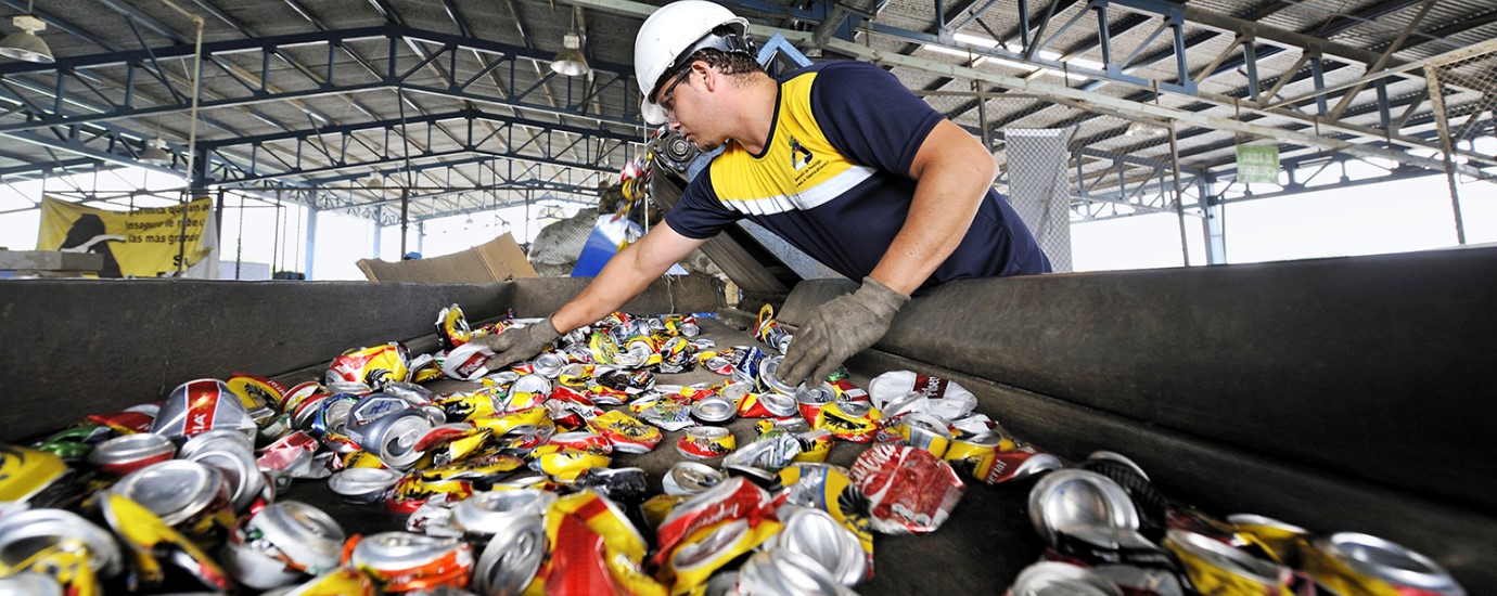 A man wearing protective gloves sorting flattened beverage cans on a conveyor belt for recycling
