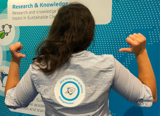 back of woman with dark hair pointing at a sticker on her back "ISC3 Global Start-up Service - Changemaker"