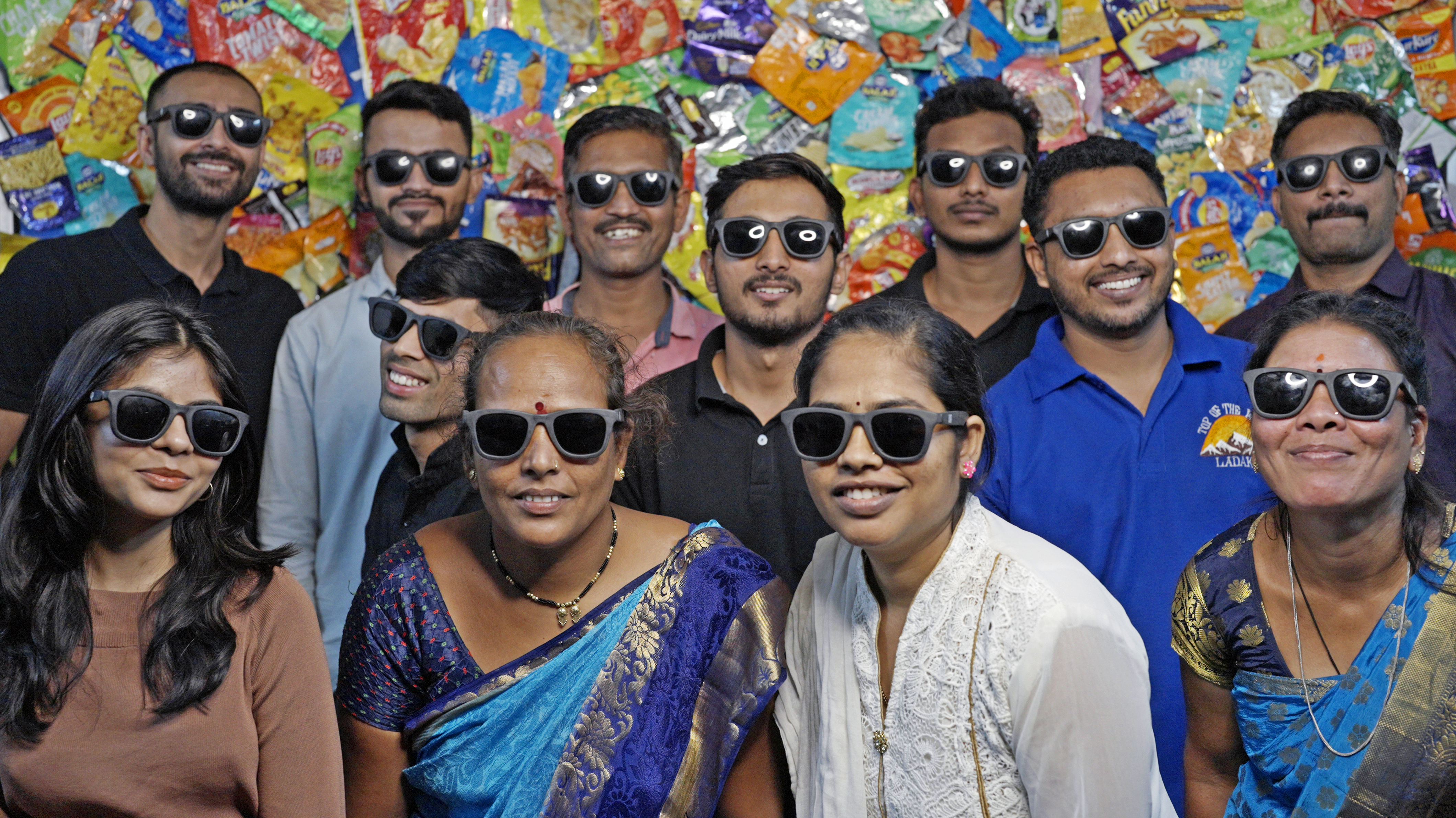 Mixed Group of Indian people with sunglasses in front of a wall decorated with colourfull chips packets