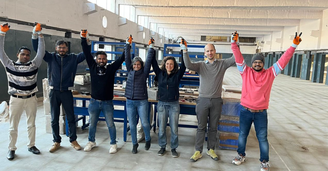 seven people in a workshop in front of work benches raising their arms