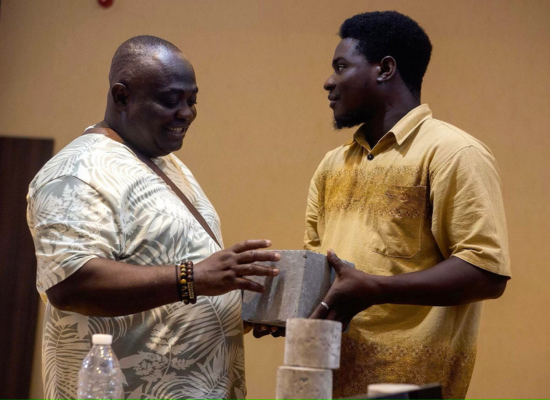 An african man presenting a cement like building block to another smiling man