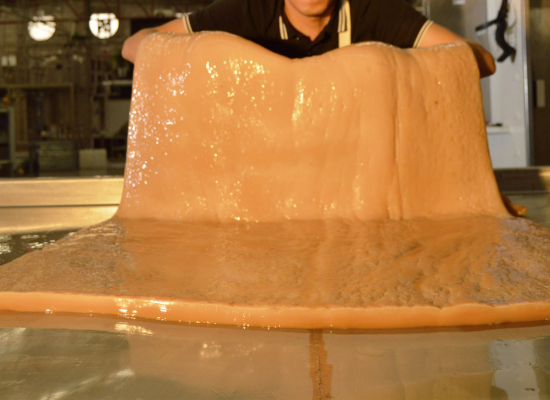 A man holding a sheet of a thick, orange, glossy and rubbery substance.