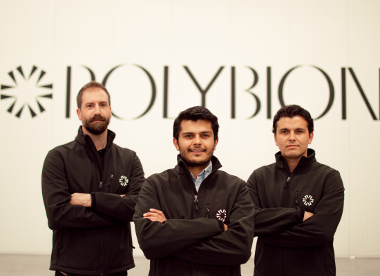 Three men in black clothing with logo looking into camera, standing before a white wall with black Polybion logo